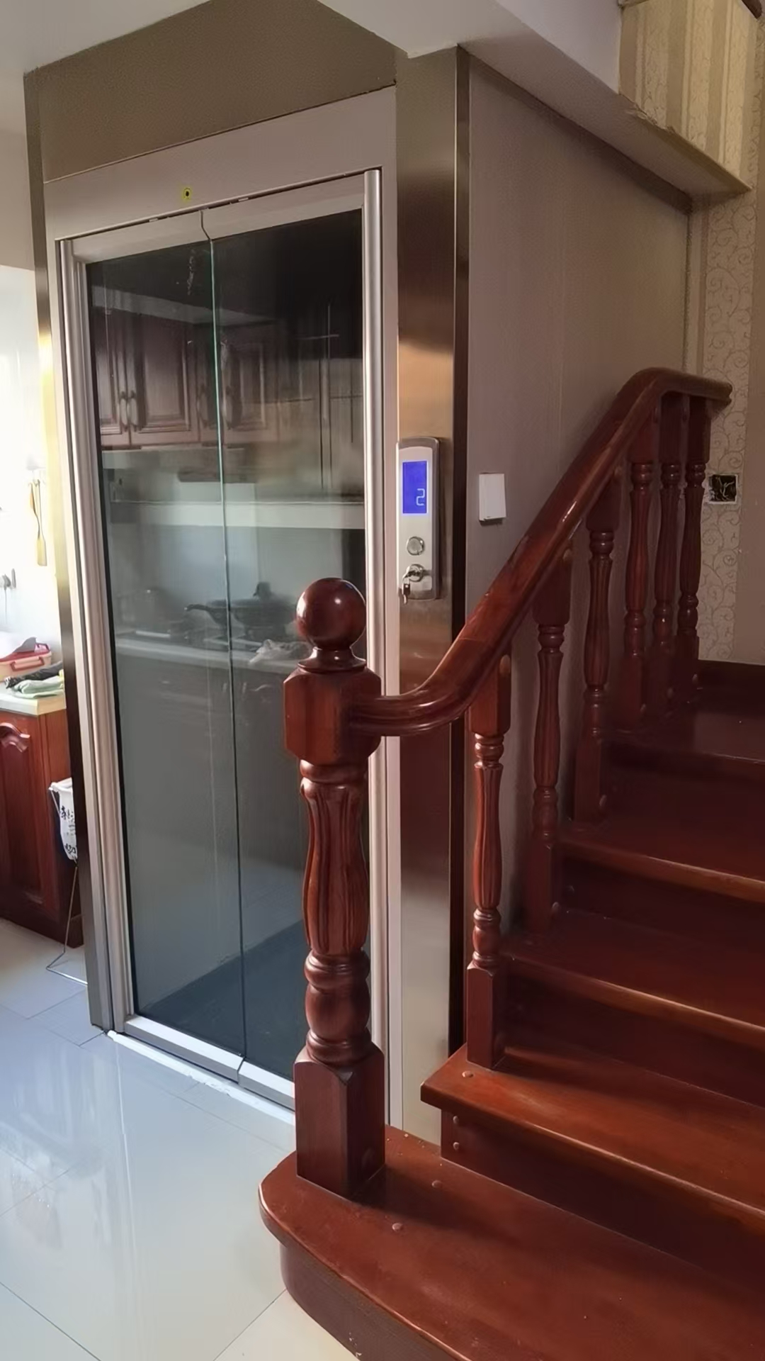 Indoor home elevator enclosure installed beside a wooden staircase