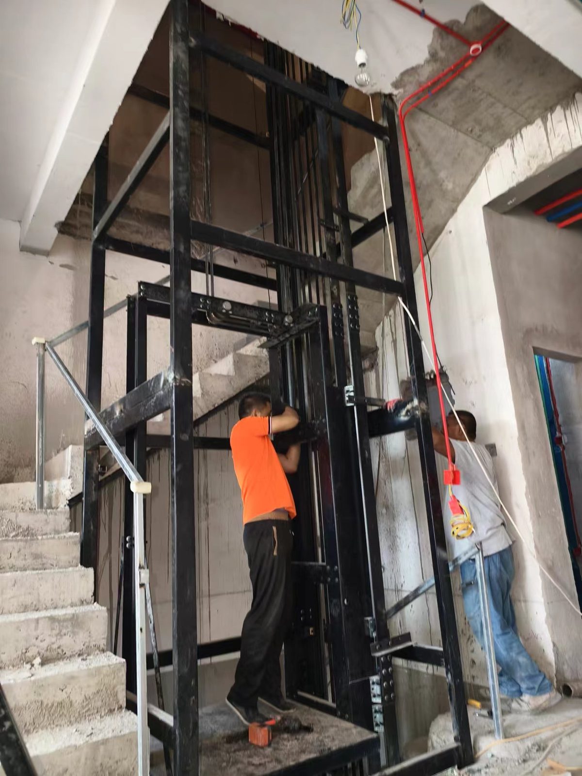 Workers installing elevator guide rails and steel frame on site